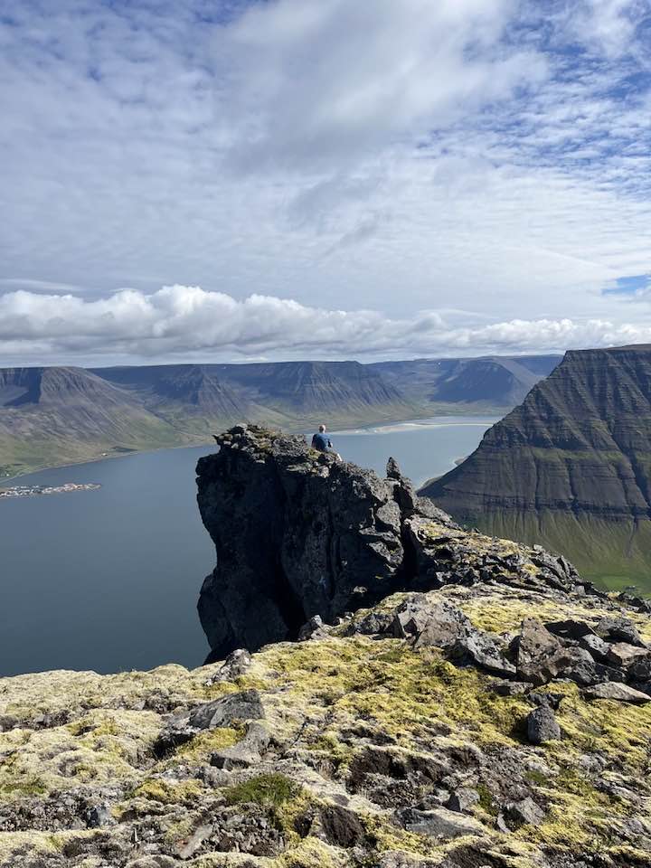 Horft yfir Sporhamarinn á toppi fjallsins. Manneskja situr á klettinum.