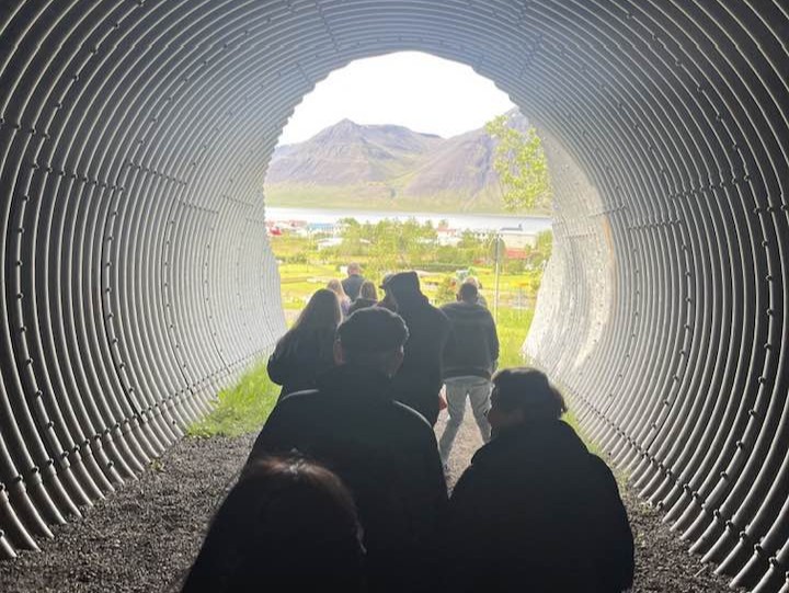 Ættarmótsgestir að ganga í gegnum rörir undir varnargarðinn á Flateyri.