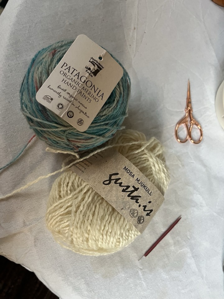 Tveir garnhnyklar, annar ljósbláyrjóttur, hinn hvítur. Við hlið þeirra eru lítil koparlituð skæri.