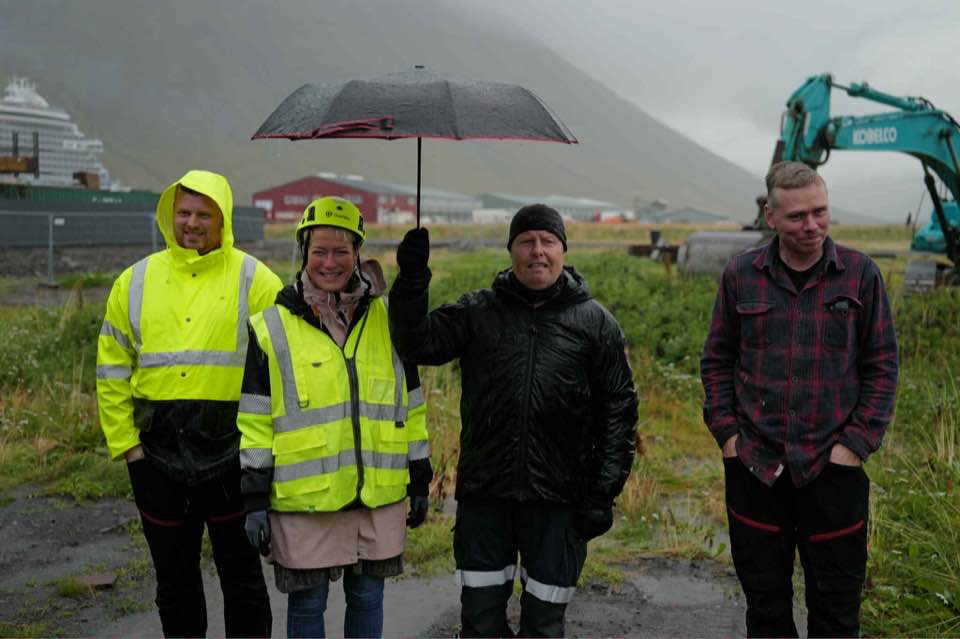 Bæjarstjóri, slökkviliðsstjóri og fulltrúar Verkhafs við skóflustunguna. Það er mikil rigning og slökkviliðsstjóri heldur regnhlíf yfir bæjarstjóra.