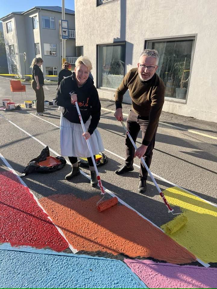 Sigga og Dúi mála regnboga á götuna fyrir framan félagsheimilið á Suðureyri.