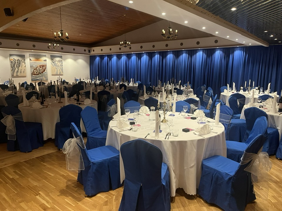 Séð yfir sal Frímúrara á Ísafirði. Bláar gardínur eru fyrir gluggum, hringborð eru dúkuð og við þá stólar með bláu áklæði.