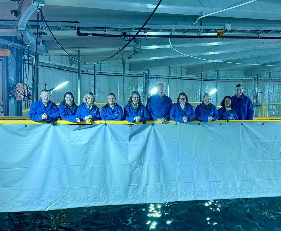 Hópurinn í bláum hlífðarfatnaði inni í eldiskví.