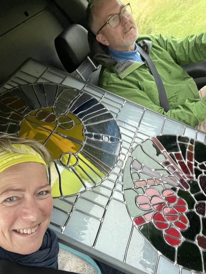 Sigga og Dúi í framsætum flutningabíls með mósaíklistaverk á milli sín.